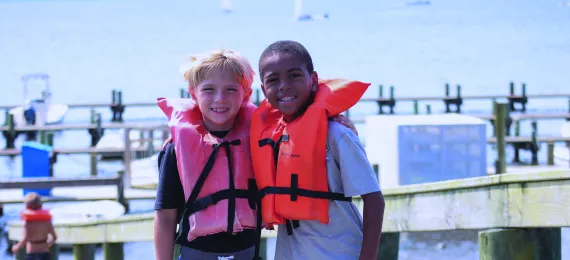 Two friends in life jackets standing by the pier