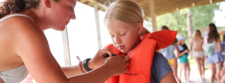 Counselor helping camper with her life jacket