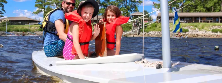 Dad and two girls enjoying time together on a sailboat at family camp