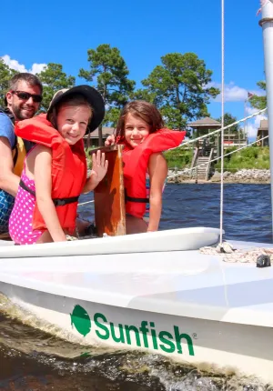 Dad and two girls enjoying time together on a sailboat at family camp